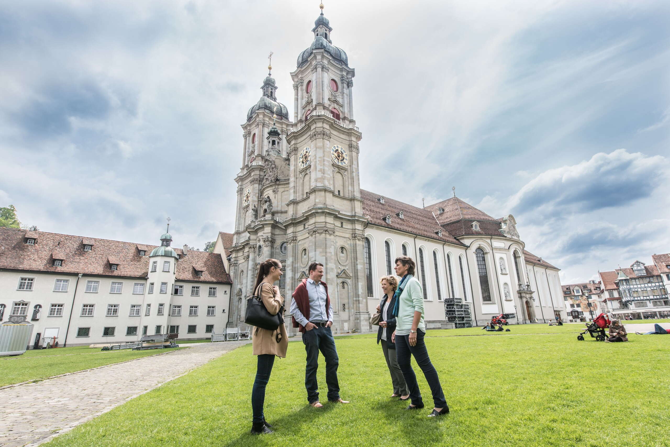Vier Menschen stehen auf dem Klosterplatz mit der Katehdrale St.Gallen im Hintergrund